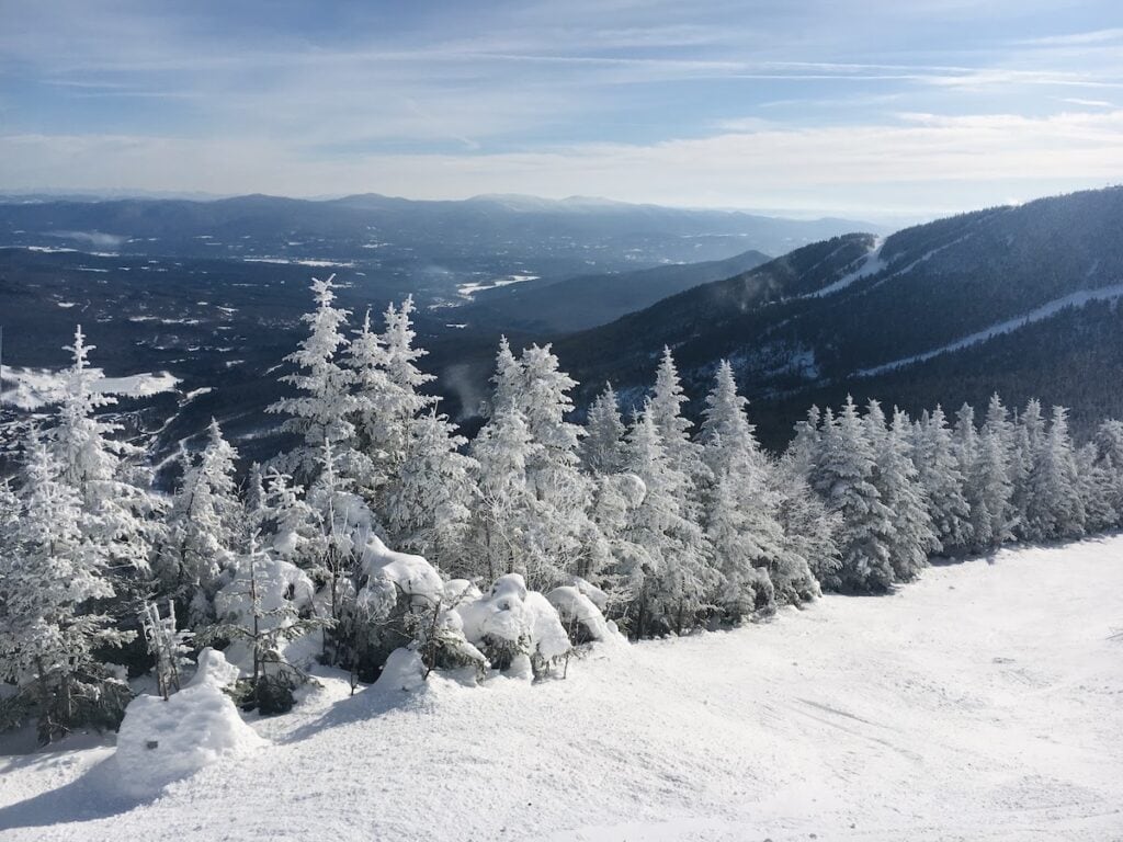Why This World Traveler Chose to Live in Vermont Over All Other Places (Including Alaska!) 5 The view from skiing an intermediate run at Stowe Mountain Resort on a clear and cold day. The sky is streaked with thin clouds and the trees in the foreground are frosted with a thick snowy cover. Mountains in the distance and other ski runs can be seen in the panoramic view.