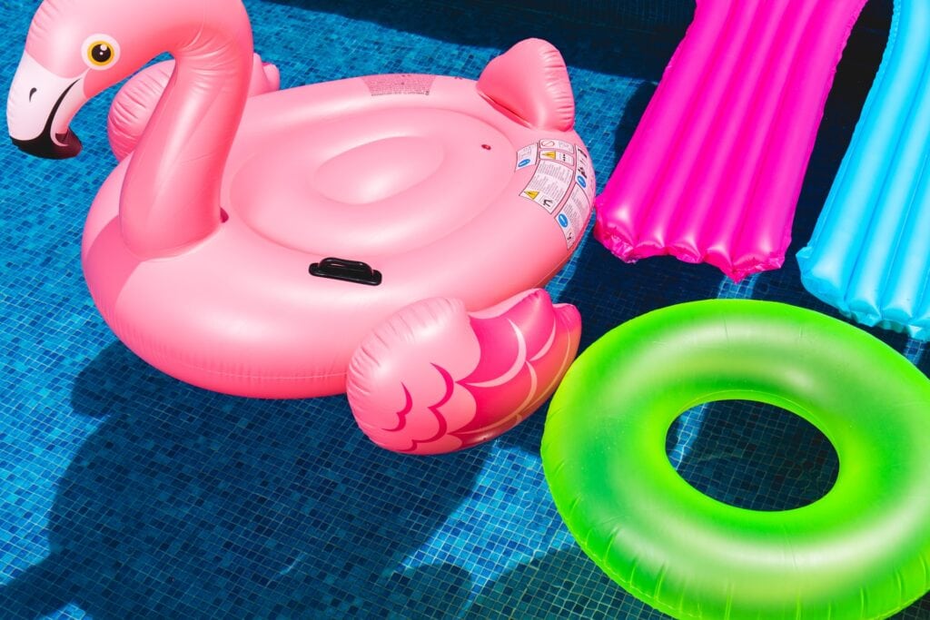 15 Best Toronto Hotels With Outdoor Pools for Summer 11 Pool with inflatable pool floaties in it. One is a pink flamingo, one is a green ring, and two are pink and blue lounge pads.
