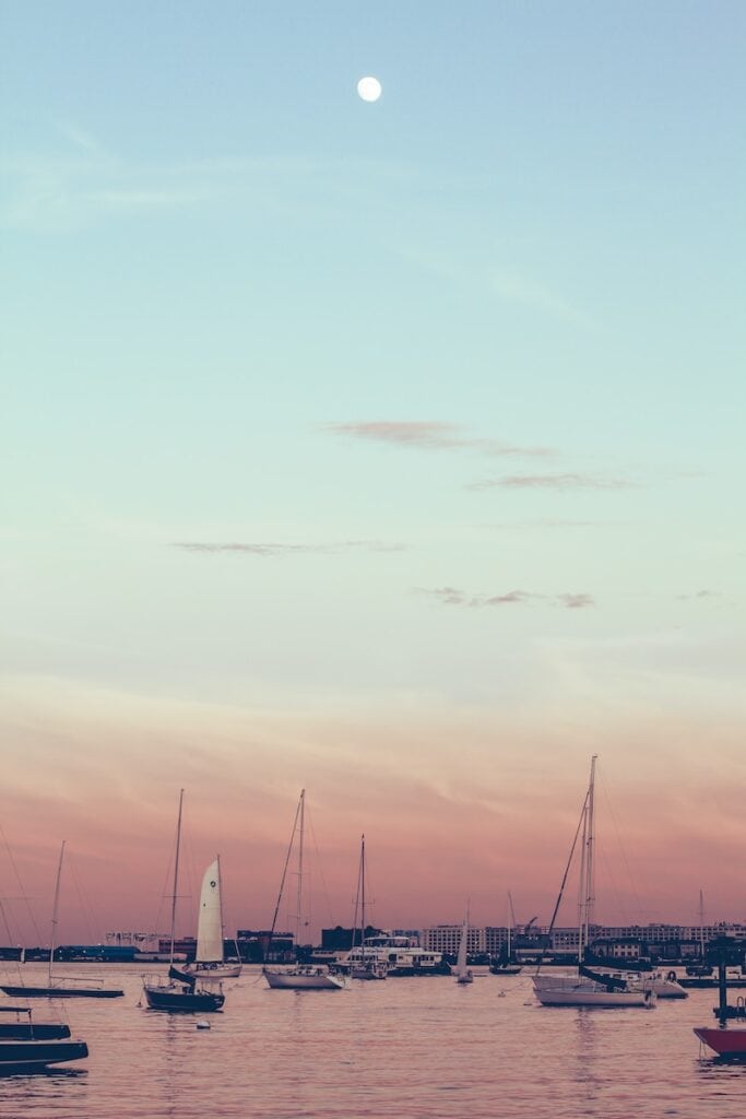 25 Pros and Cons of Living in Boston in 2024 6 Sailboats on the harbour in Boston at sunrise.