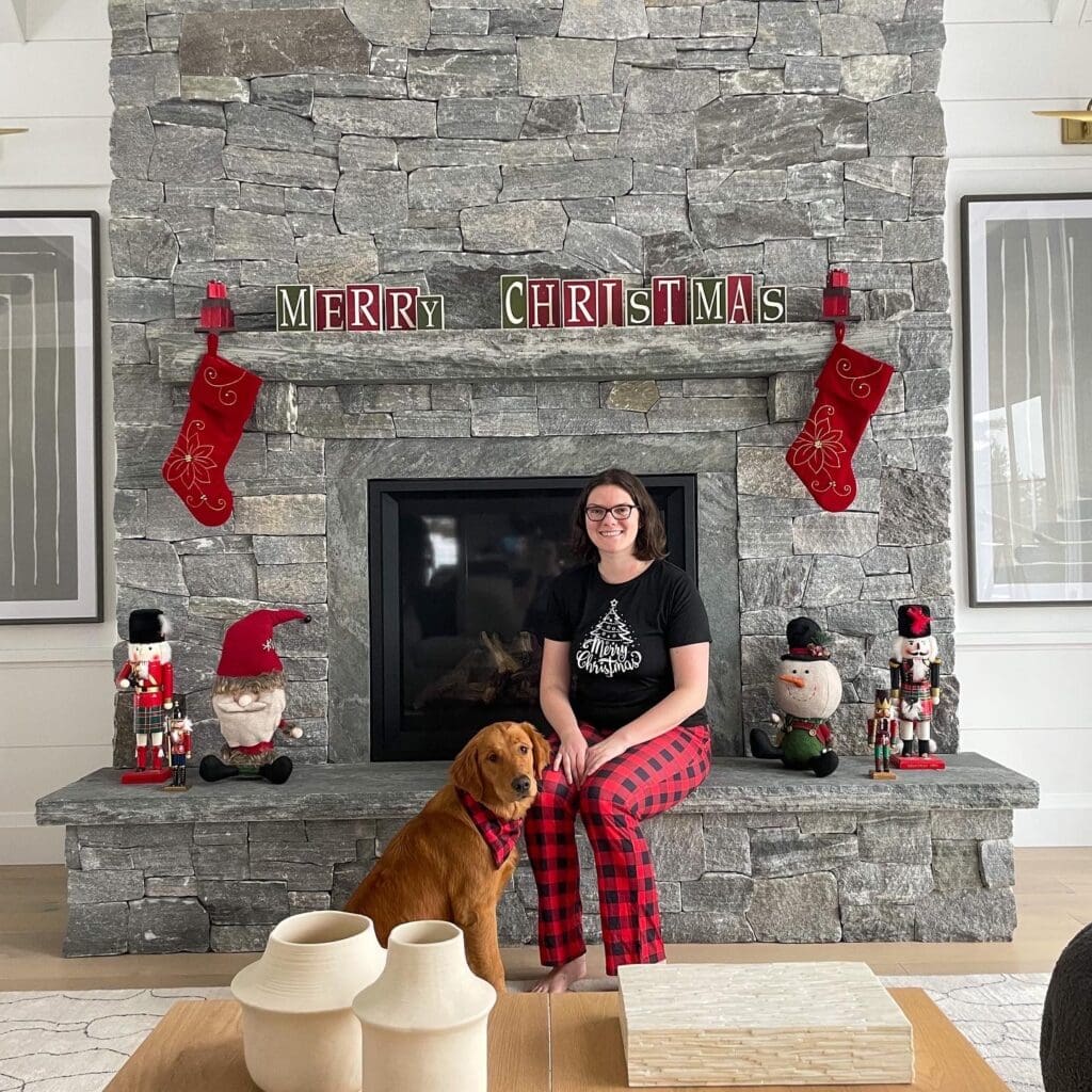 It’s Ok to Spend Christmas Alone (From Someone Who Has!) 8 Nina sitting on a fireplace that says "Merry Christmas" beside her golden retriever. They're wearing matching plaid PJs.