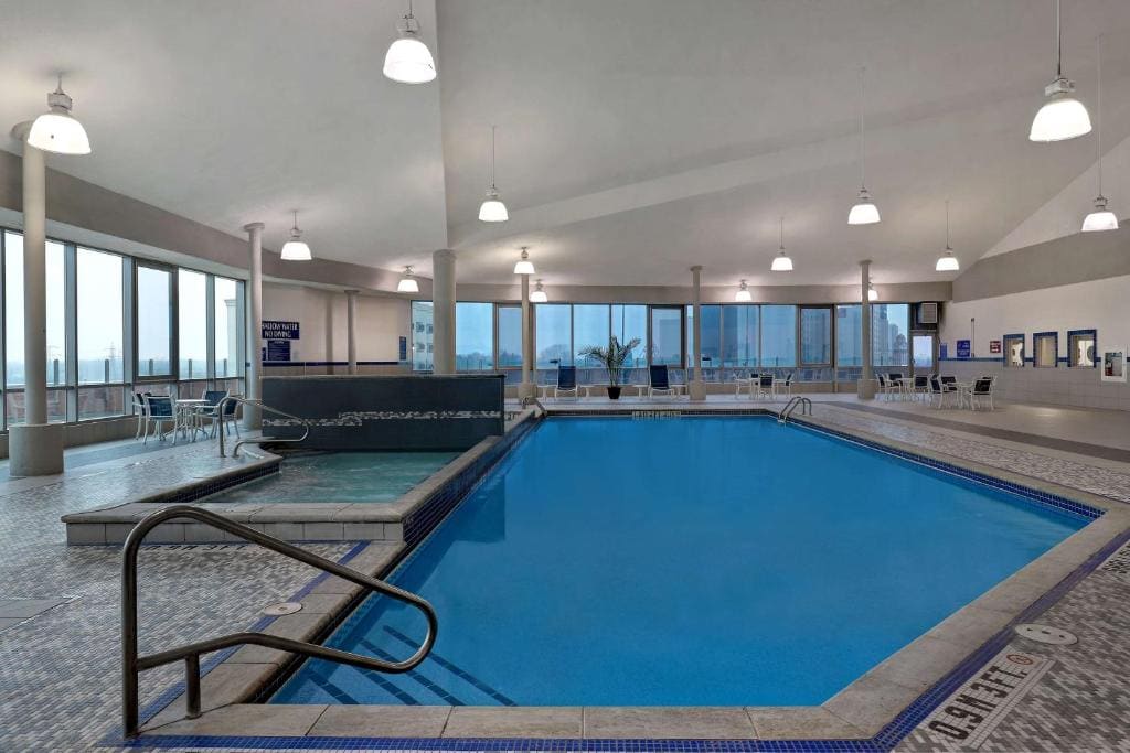 15 Luxurious Niagara Falls Resorts (2024 Guide) 14 2 indoor pool with railings at Embassy Suites Fallsview surrounded bu lounge chairs and huge windows that has a view the city and niagara