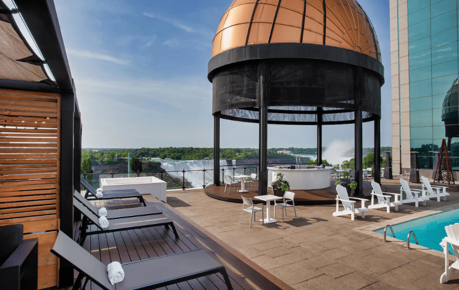 15 Luxurious Niagara Falls Resorts (2024 Guide) 12 outdoor rooftop pool with lounge chairs and a circular bar with a dome roof at Sheraton Fallsview Resort with a view of Niagara falls,