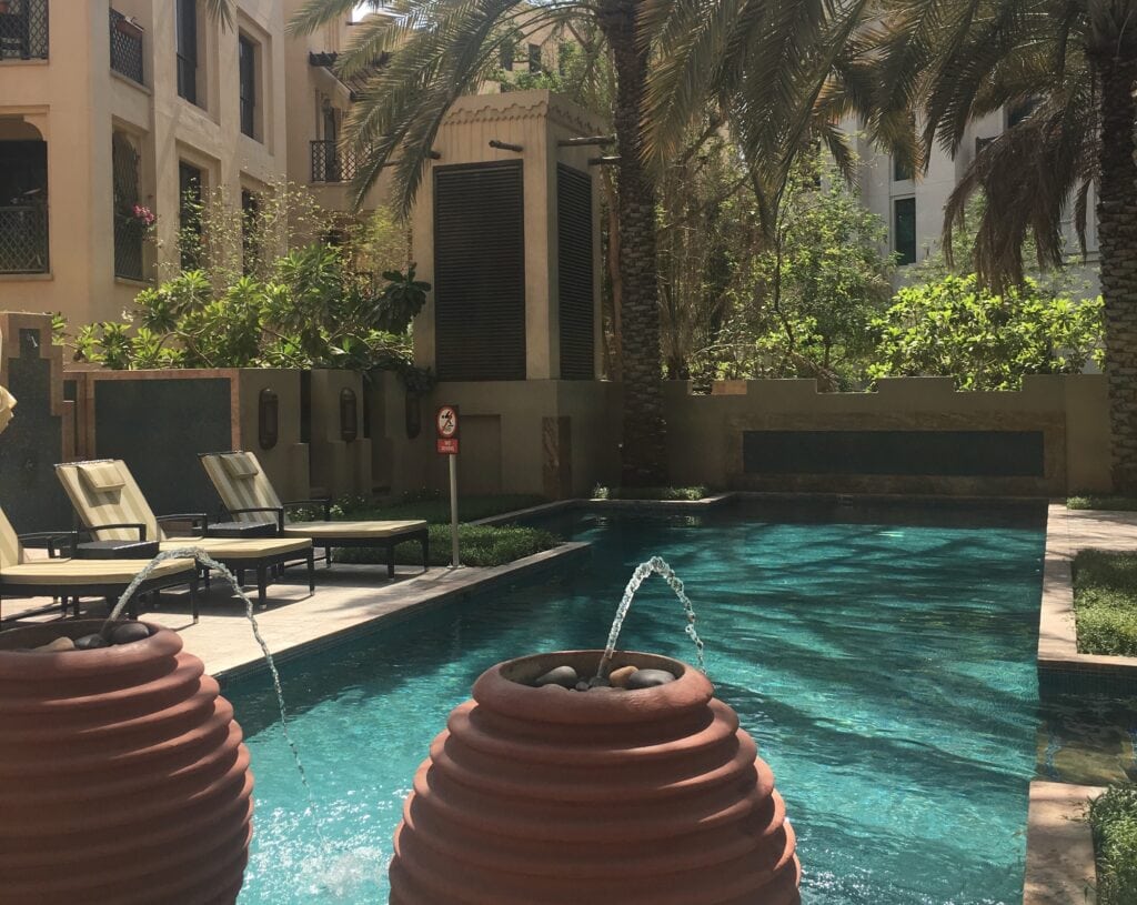 This Expat Left Teaching in Japan for Living in Dubai. Here's Why! 2 The pool at Danni's apartment. It has fountains of water coming out of clay pots into teal waters with palm trees.
