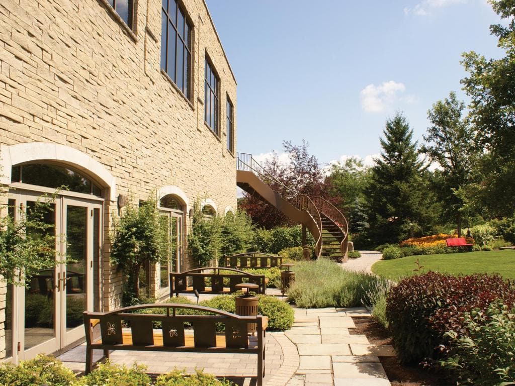 15 Luxurious Niagara Falls Resorts (2024 Guide) 11 garden outside a huge brick building with double doors with benches and a staircase outsided. Lots of trees on a sunny day at White Oaks Conference & Resort Spa