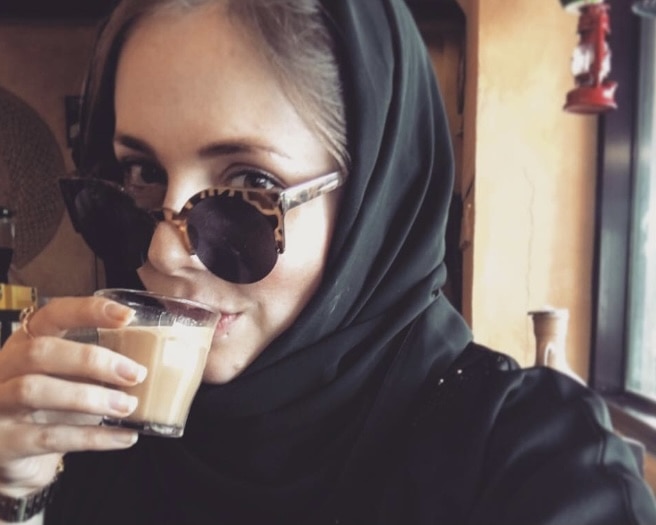 This Expat Left Teaching in Japan for Living in Dubai. Here's Why! 4 Dani drinking karak, a traditional spiced tea drink, in a small glass cup while wearing sunglasses.