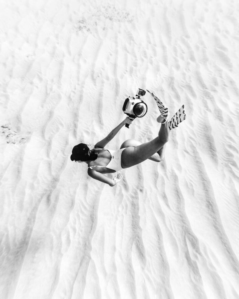 17 Best Snorkeling Tours in Puerto Rico in 2024 6 Black and white faceless slim female wearing swimsuit and flippers snorkeling above sandy sea bottom in transparent waters and carrying camera in waterproof cover