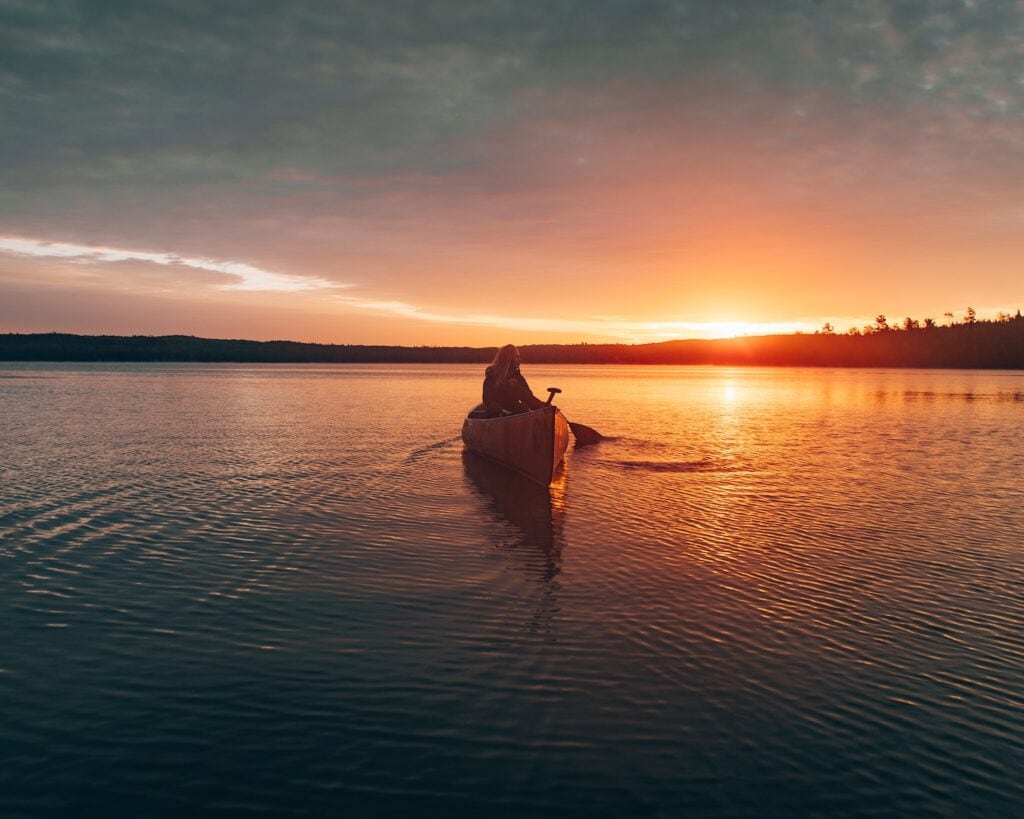 These are the Best Outdoor Adventures Near the US/Canada Border 2 person sailing canoe during sunset in Boundary Waters Canoe Area Wilderness.