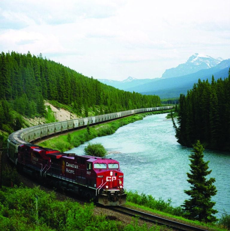 A red Canadian Pacific train crossing the Stoney Creek Bridge amidst lush greenery and mountainous terrain, showcasing the iconic rail infrastructure of Canada.