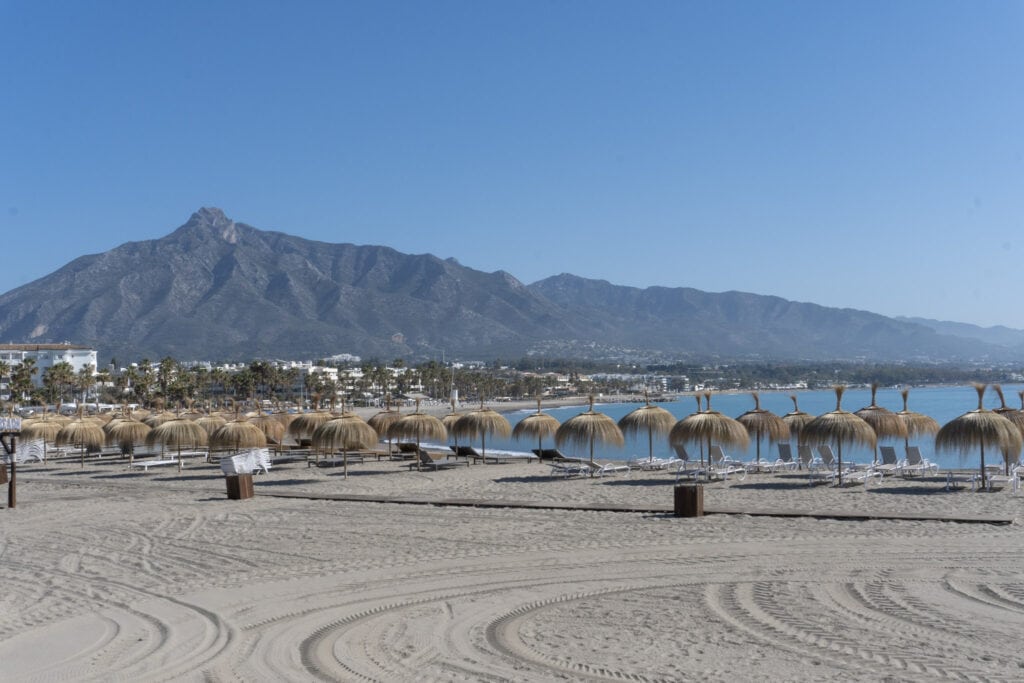 Discover Life Beyond the Tourist Trails in Spain's Coastal Towns Through a Local's Eyes 7 Pristine beach in Marbella with thatched sun umbrellas and a view of the Sierra Blanca mountains, a highlight from Cristina's Costa Del Sol experience.