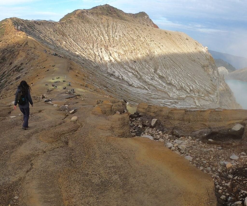 This Expat Traded London Life for Bali's Laidback Tropics 7 Abi hiking along a volcano's ridge in Bali with the winding edge of a mountain trail leading her closer to the top.