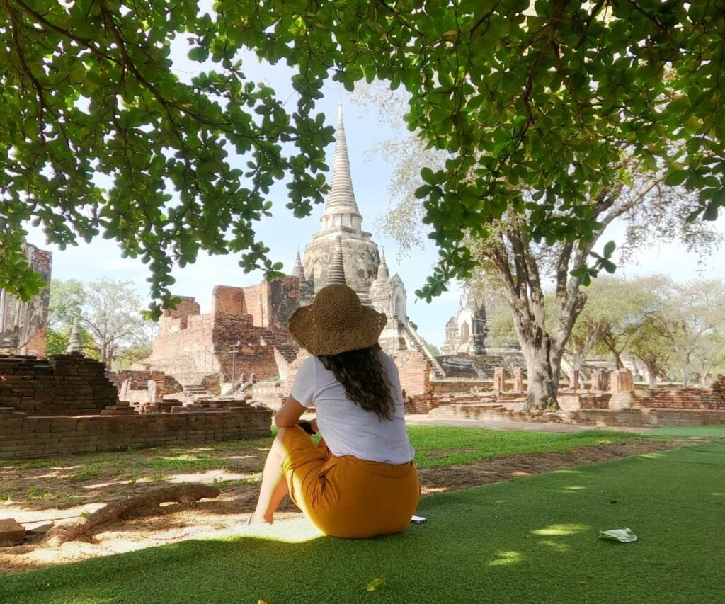 This Expat Traded London Life for Bali's Laidback Tropics 9 Abi sitting with her back facing the camera wearing a straw hat and yellow skirt in front of Bali temples.