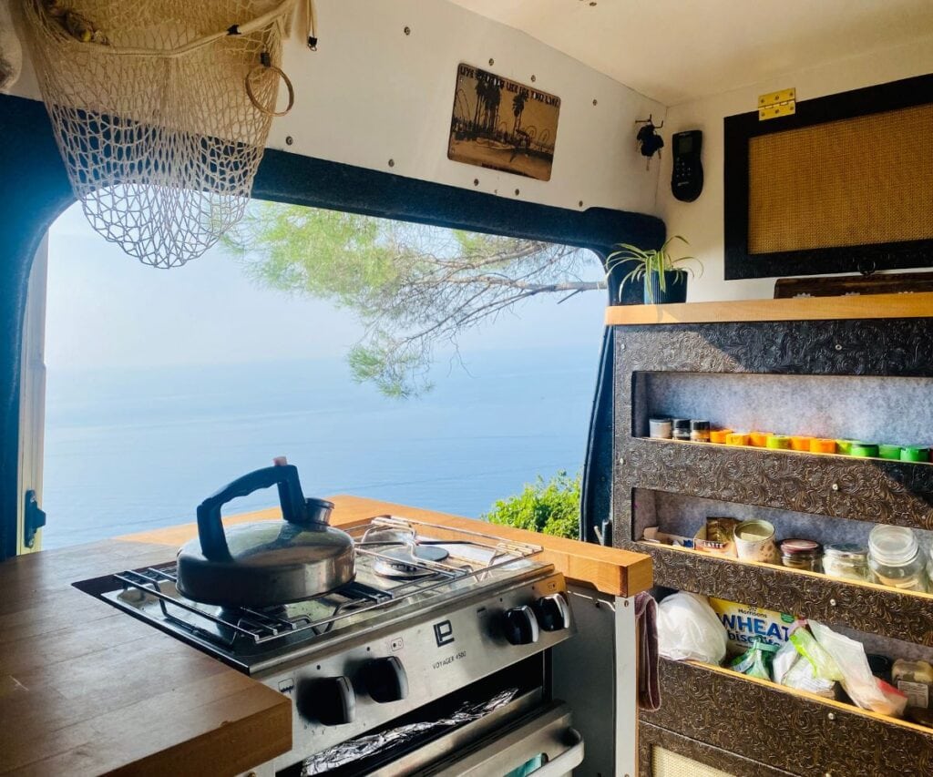 This Expat Traded London Life for Bali's Laidback Tropics 8 View from the interior of Abi's campervan with a kettle on the stove and a spice rack hanging up in front of the door. The door is open to show a view of the ocean.