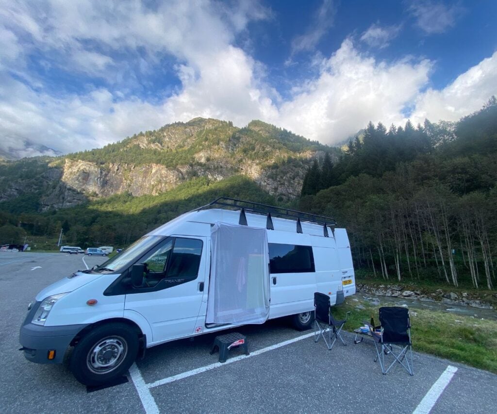 This Expat Traded London Life for Bali's Laidback Tropics 4 White campervan in the mountains at a parking spot with two camping chairs outside of it and a bug netting over the door area.
