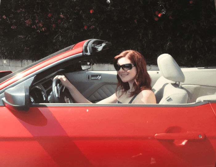 20 Reasons Not to Live in the US (2024) 9 Nina wearing sunglasses riding a red convertible car.