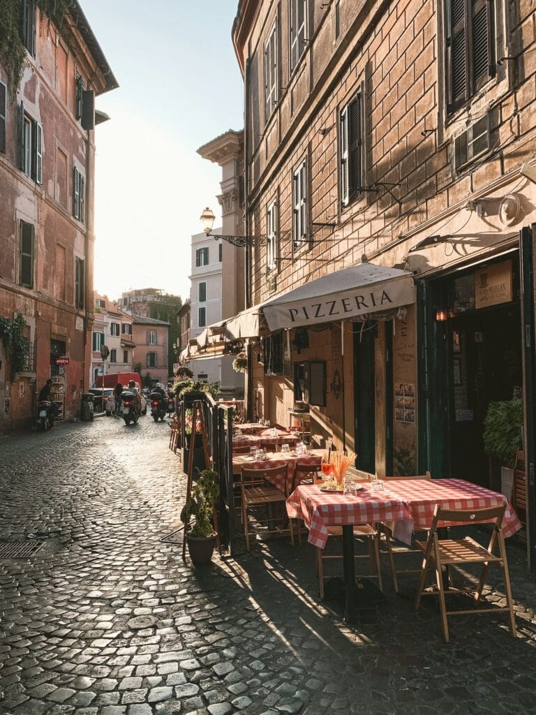 14 Top Freelance Visa Countries To Live And Work In 2024 6 A pizza place in the streets of Italy. There are tables covered with red checkered table clothes.