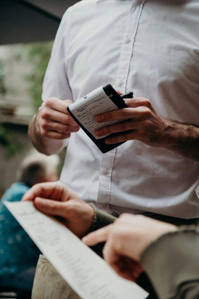 20 Reasons Not to Live in the US (2024) 14 A waiter with his notepad waiting while the customer checks the bill.