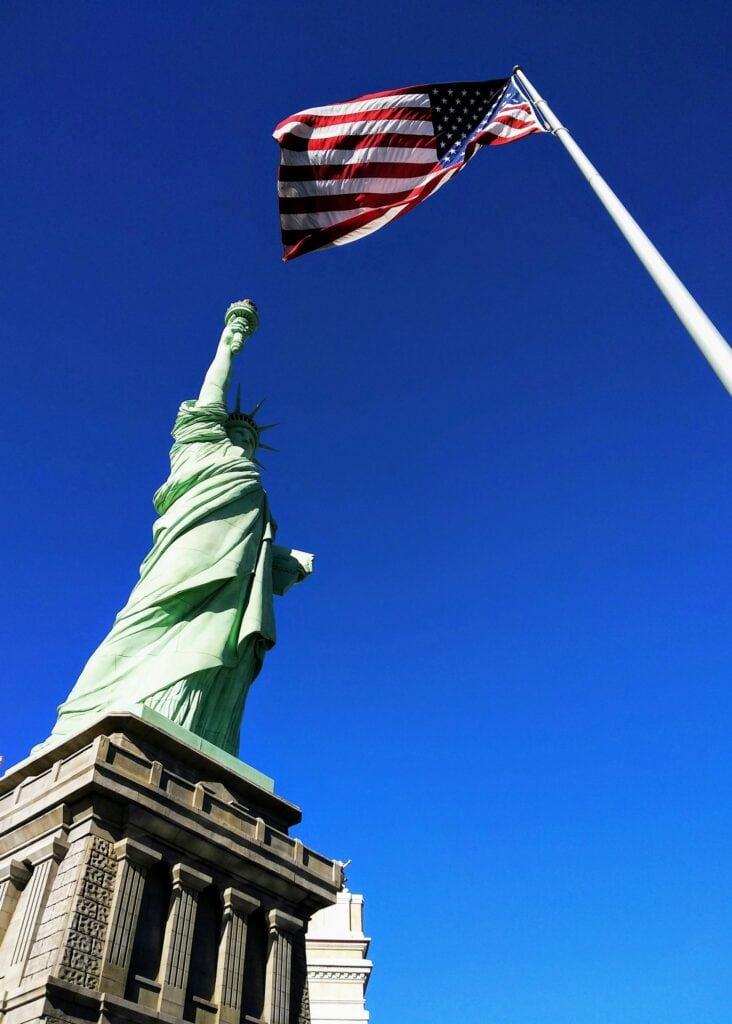 20 Reasons Not to Live in the US (2024) 21 The Statue of Liberty beside the American flag.