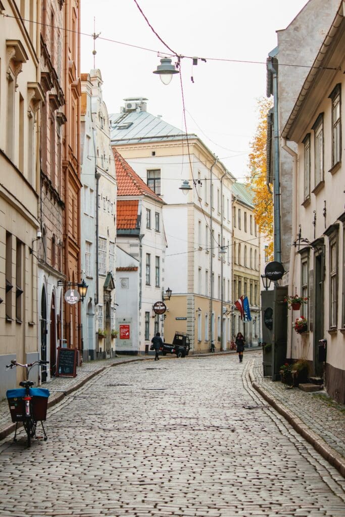 ALL European Countries With Digital Nomad Visas (2024) 13 a cobblestone street in Latvia with a bicycle and two people walking in opposite directions