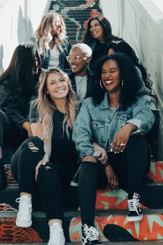20 Reasons Not to Live in the US (2024) 6 A group of women of different race and color united and smiling happily while sitting at a stair.