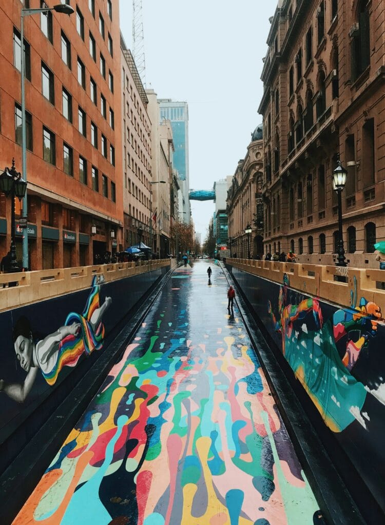 13 Countries That Will Pay You To Move There (Expat’s Picks) 3 An undergrufh walkway with floor and wall murals between two brown buildings in Chile.
