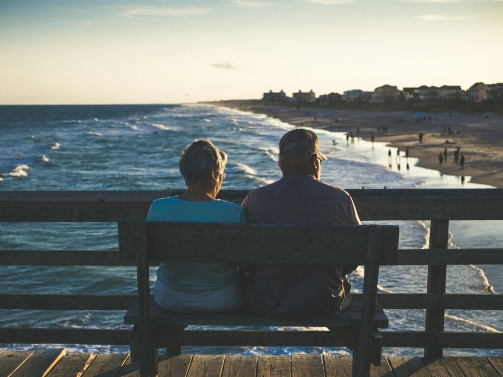 Retiring In Ireland: Pros And Cons (From an Expat!) 4 An old man and woman sitting on bench in front of beach in Ireland.