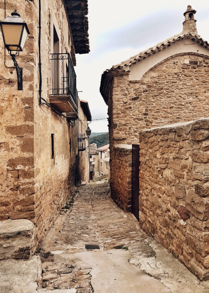 13 Countries That Will Pay You To Move There (Expat’s Picks) 6 a cobblestone street in Spain set in a narrow alley of old stone buildings.