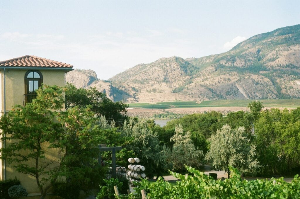 15 Best Places to Retire in Canada (From a Local Canadian!) 14 An old building in South Okanagan surrounded with trees and a view of the mountains in the back.