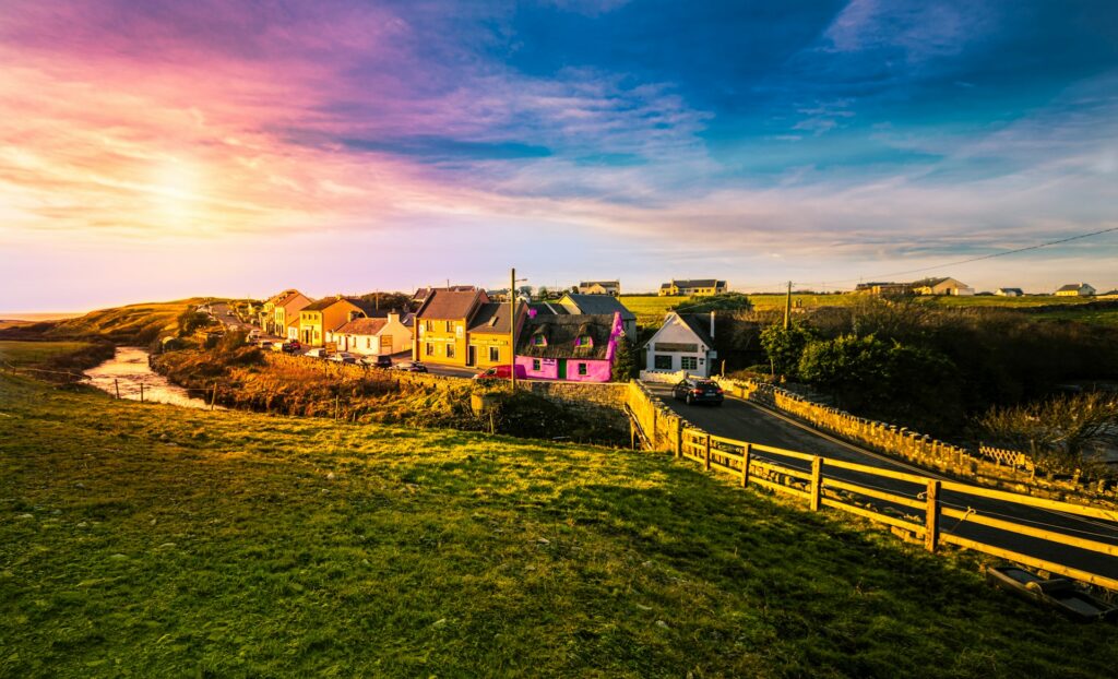 Retiring In Ireland: Pros And Cons (From an Expat!) 2 A row of colorful houses beside the road under a colorful sky in Ireland.