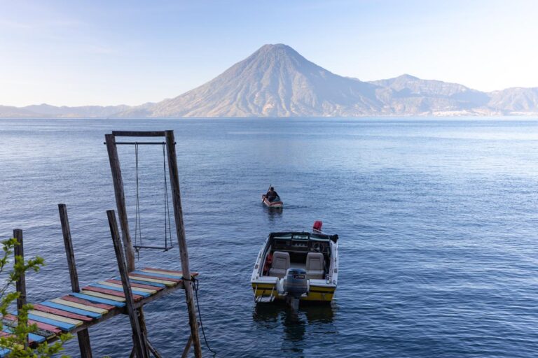 9 Easiest Jobs to Do While Traveling 8 Serene view of Lake Atitlan with the imposing San Pedro Volcano in the background, a wooden dock in the foreground, and a boat heading towards the horizon.