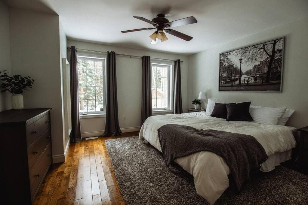 20 Top Airbnb Cottages in Muskoka for an Epic Getaway 19 a bedroom with a cozy interior design and white bedsheet and tow windows looking out to a snowy day.