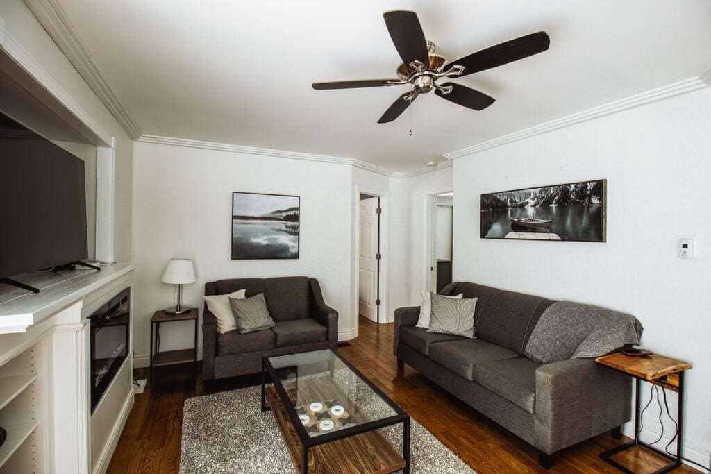 20 Top Airbnb Cottages in Muskoka for an Epic Getaway 20 the living room of a cozy cottage retreat, plus a couple of small couches, a coffee table and a black fan