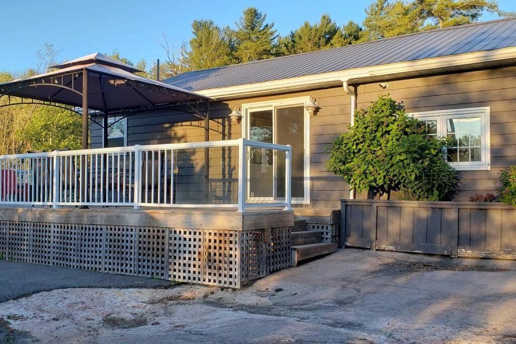 20 Top Airbnb Cottages in Muskoka for an Epic Getaway 12 Muskoka Getaway Exterior. A single-story house with a deck and a metal roof shelter at sunset.