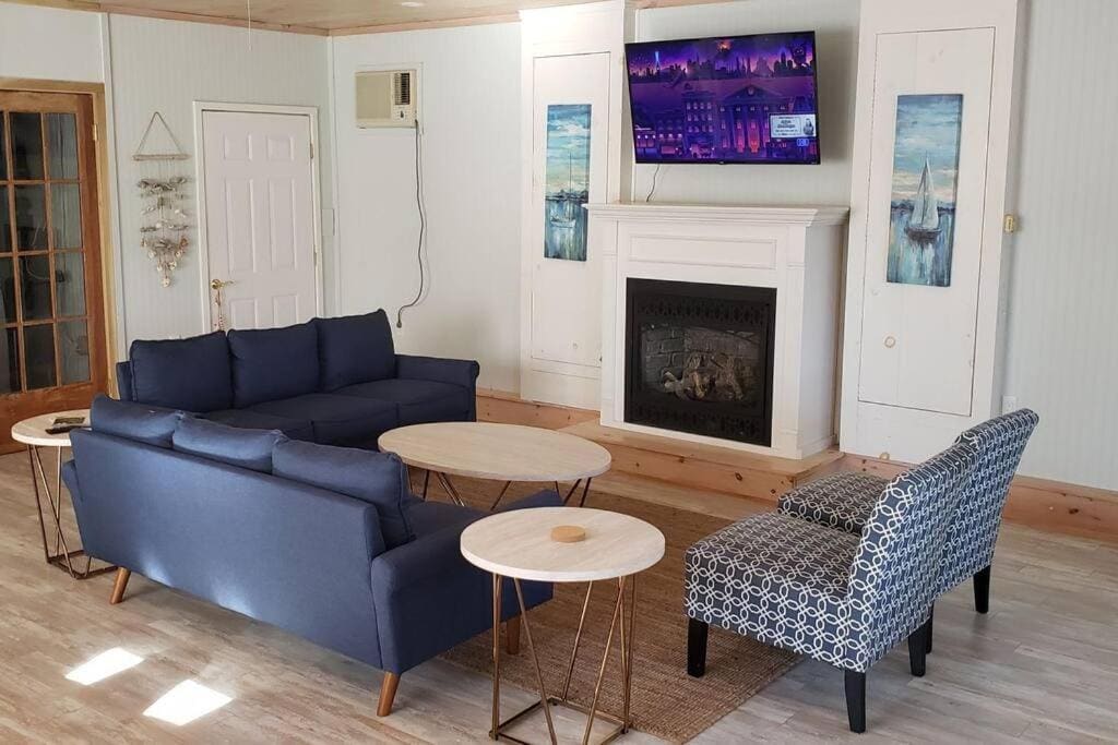 20 Top Airbnb Cottages in Muskoka for an Epic Getaway 10 Muskoka Getaway Living Room. A cozy living room with a blue sofa, patterned armchair, wooden coffee tables, and a television mounted above a fireplace.