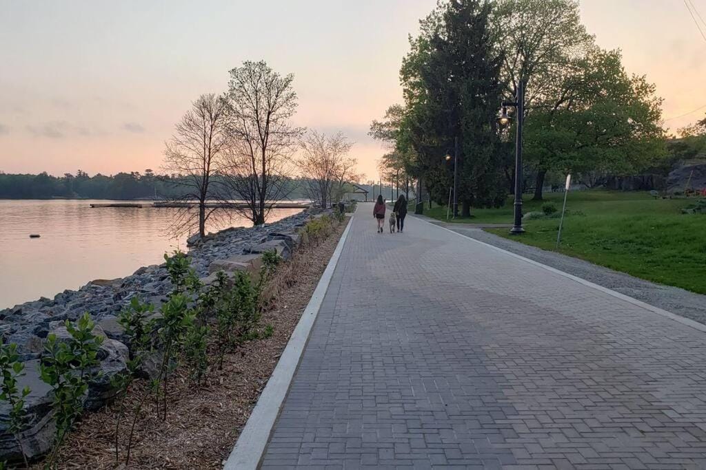 20 Top Airbnb Cottages in Muskoka for an Epic Getaway 11 Muskoka Getaway View. People walking on a paved path along a river at dusk.