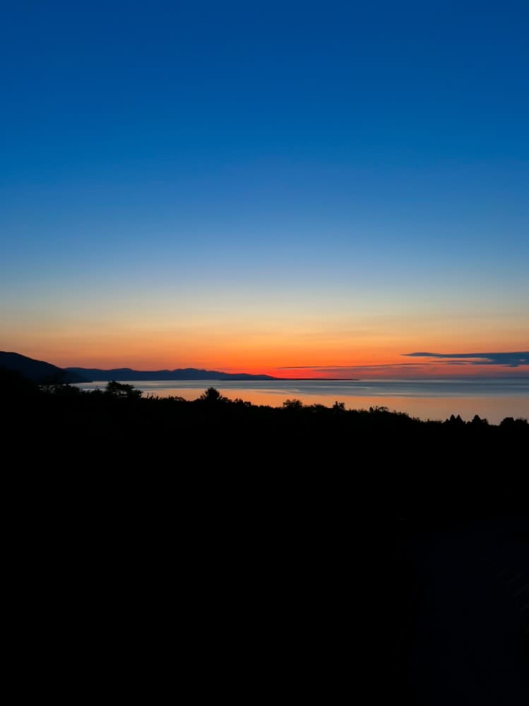 My 4 Day Charlevoix Itinerary to Recharge in Quebec 5 Brilliant orange and blue sunrise over the calm St. Lawrence River with distant silhouettes of mountains and trees. Early morning views like this are a peaceful highlight of any stay in Charlevoix.