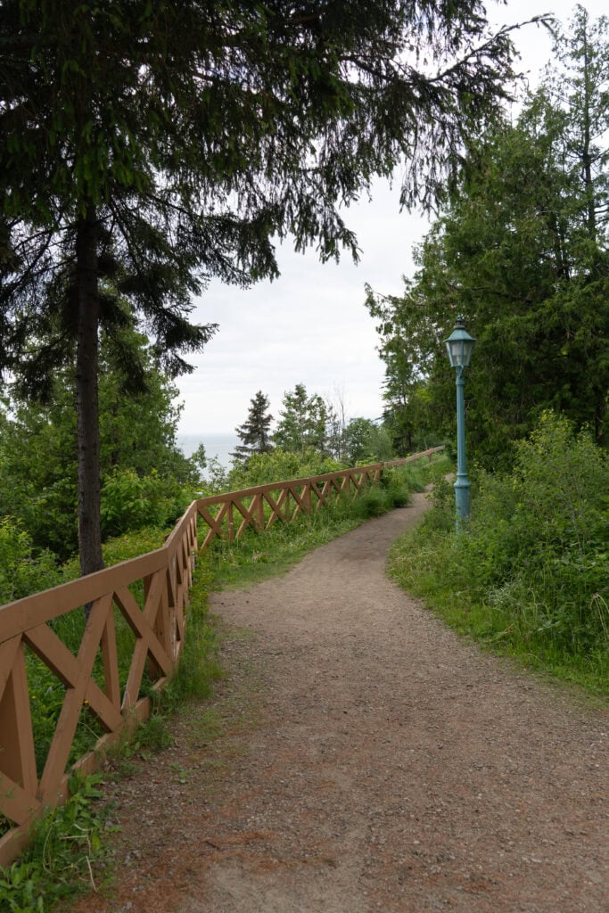 My 4 Day Charlevoix Itinerary to Recharge in Quebec 14 Quiet gravel walking path lined with wooden fencing and an old-fashioned lamppost, surrounded by green trees behind the Fairmont Le Manoir Richelieu. A peaceful trail for sunset strolls.