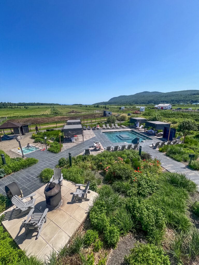 My 4 Day Charlevoix Itinerary to Recharge in Quebec 10 Aerial view of the Nordic spa pools surrounded by lounge chairs, gardens, and open farmland with mountains in the distance at Le Germain. A relaxing wellness stop during a Charlevoix itinerary.